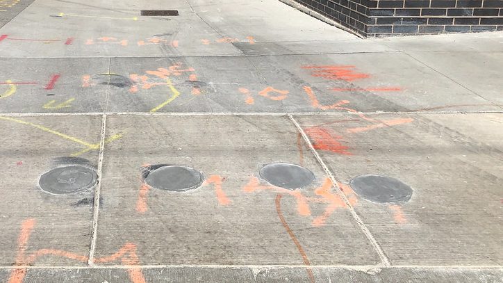 A marked sidewalk showing orange communications, red electric and yellow gas locate paint alongside four patched vacuum-excavation test holes